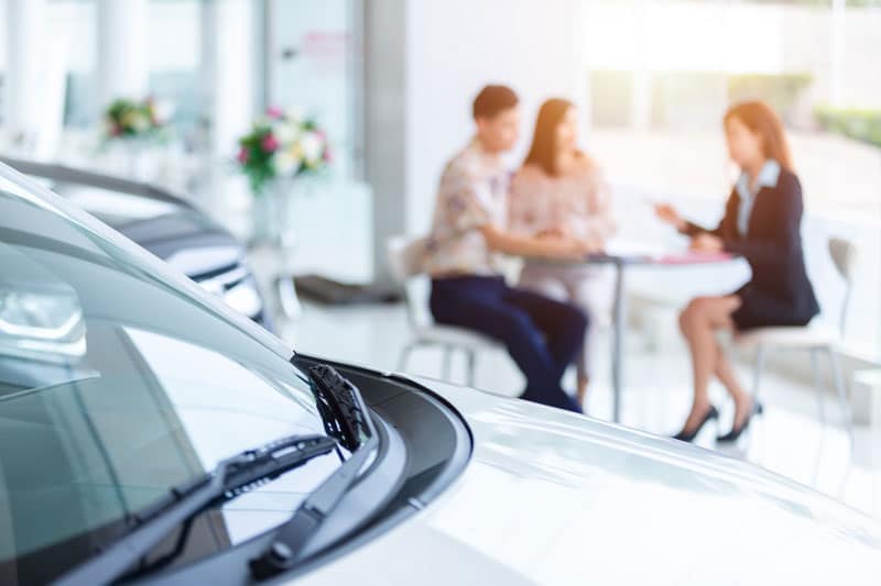 Professionnelle de l'automobile qui échange avec deux personnes qui souhaitent acheter une Porsche