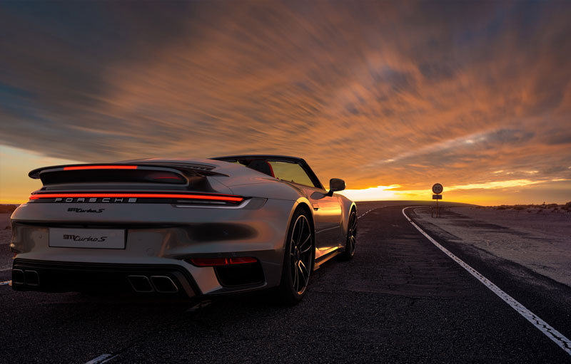 Zoom sur une Porsche Turbo qui circule sur une route lors d'un coucher de soleil 