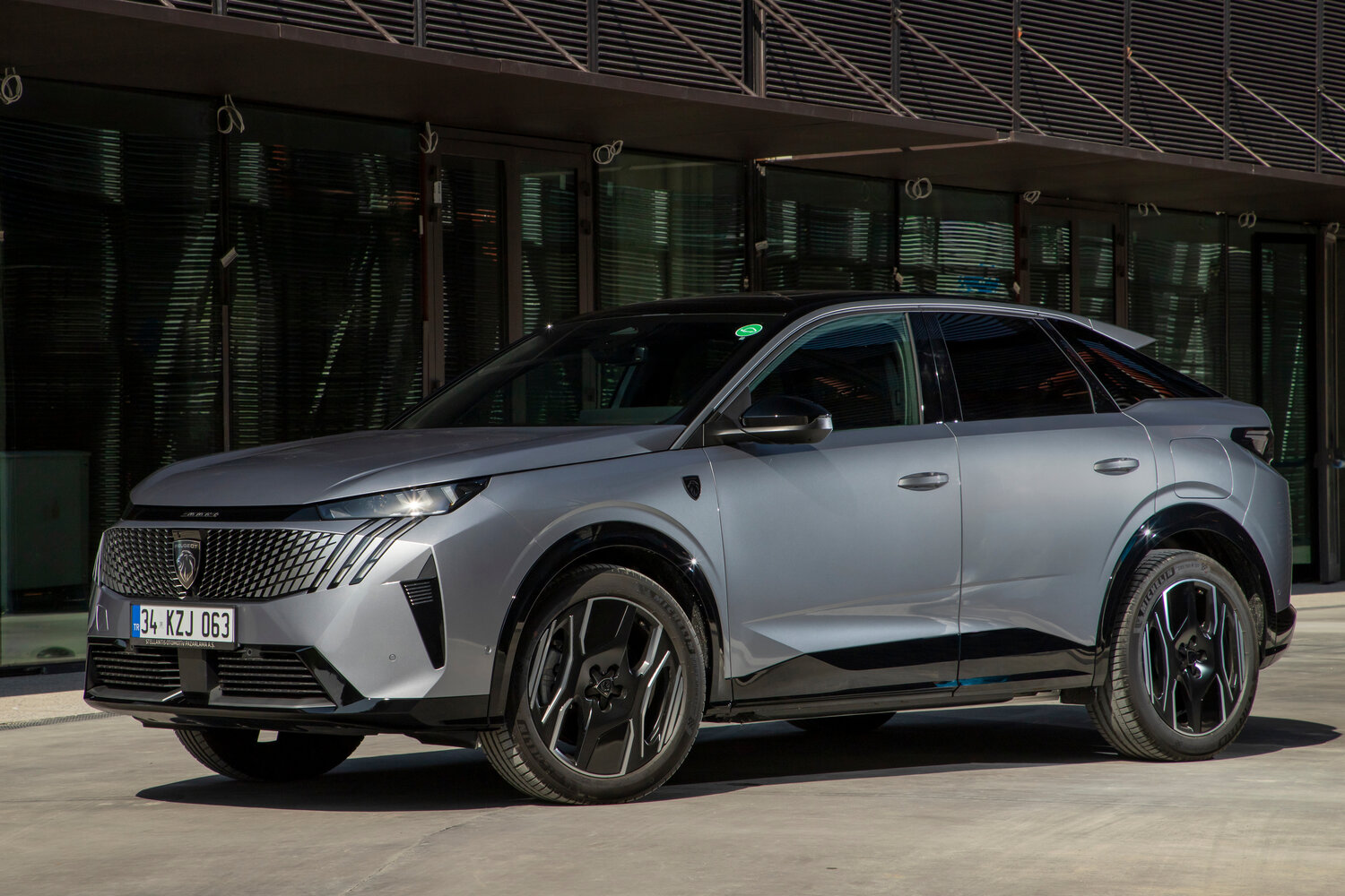 SUV coupé Peugeot gris à toit noir, calandre sombre et jantes 20 pouces, garé devant un bâtiment vitré